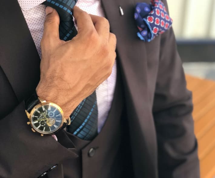 the man touches his tie and wiers the gold watch on his palm